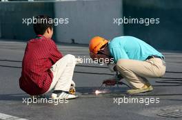 18.07.2004 Shanghai, China,  DTM, Sunday, Local worksman are welding the manhole covers after the accident of Bernd Mayländer (GER), CLK AMG-Mercedes, Mercedes CLK-DTM at the first start. All covers on the entire circuit were welded which caused a delay of about 4 hours - DTM Season 2004 at Pu Dong Street Circuit Shanghai (Deutsche Tourenwagen Masters)