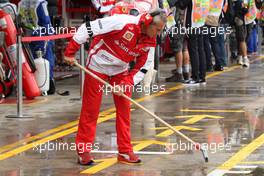 Ferrari mechanic sweeps rain water from the pit box.
